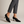 Ariane suede kitten heel pumps in Black worn with cropped gray trousers on a light gray studio backdrop