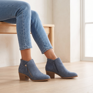 Beatrice suede ankle boots in Blue worn seated on a pale oak bench