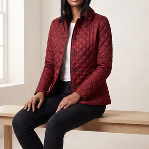 Belinda quilted jacket in Dark Red worn seated on an oak bench