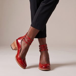 Clarisse block heel pumps in Red worn with ankles crossed on a light gray studio backdrop