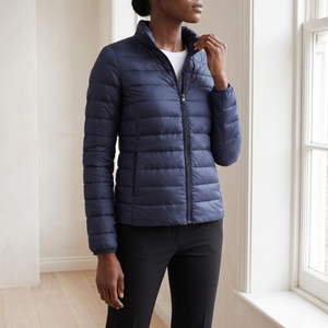 Clementine quilted down jacket in Navy Blue with the stand collar, worn by a window