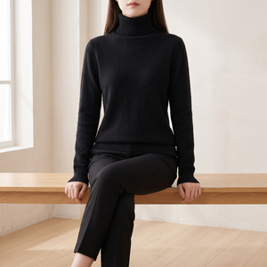 Cressida cashmere turtleneck sweater in Black worn seated on an oak bench