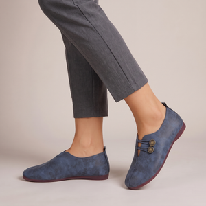 Elinor round toe flats in Blue worn with cropped gray trousers on a light gray studio backdrop