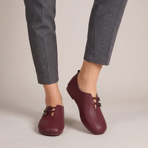 Elinor round toe flats in Burgundy worn with cropped gray trousers on a light gray studio backdrop