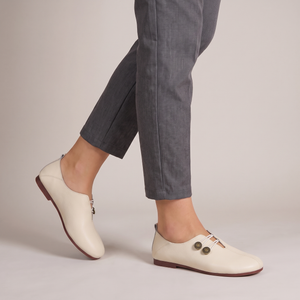 Elinor round toe flats in Ivory worn with cropped gray trousers on a light gray studio backdrop