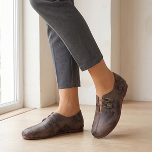 Elinor round toe flats in Dark Brown worn with cropped gray trousers on a pale oak floor by a window