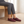 Elinor round toe flats in Burgundy worn by a woman seated on a pale oak bench