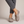 Elinor round toe flats in Taupe worn with cropped gray trousers on a light gray studio backdrop
