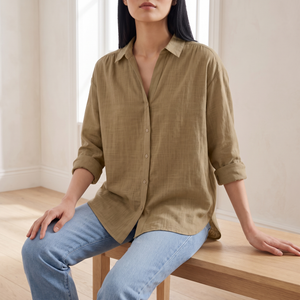Francesca linen blend button down shirt in Khaki, seated on an oak bench in a bright room