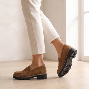 Gloria suede penny loafers in Brown mid stride on an oak floor, showing the lug sole