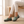 Gloria suede penny loafers in Sage worn seated on an oak bench