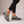 Gloria suede penny loafers in Sage worn with black cropped trousers on a light gray studio backdrop