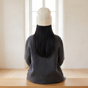 Hattie knit beanie in White worn with a gray wool coat, seen from behind on an oak bench by a window