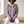 Honorine floral yoke cardigan in Lavender, seated on an oak bench