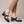 Hortense leather Mary Jane pumps in Black with cropped camel trousers on a light gray studio backdrop