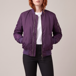 Imelda nylon bomber jacket in Purple worn open with both hands in the front pockets on a light gray studio backdrop