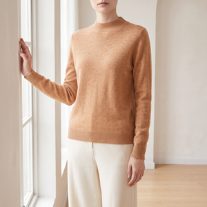 Woman in the Imogen cashmere sweater in Camel standing by a window in a bright room