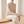 Woman seated on a pale oak bench wearing the Imogen cashmere sweater in Beige and cream trousers