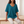 Jemima loose scoop neck blouse in Teal worn seated on an oak bench