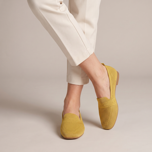Lorelei slip on flats in Yellow worn with ankles crossed on a light gray studio backdrop