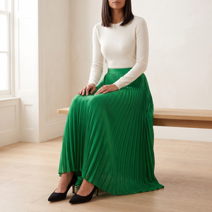 Margot pleated maxi skirt in Green worn seated on a pale oak bench