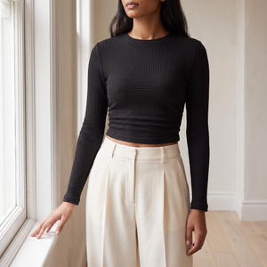 Maribel long sleeve crop top in Black, standing by a window in a bright room