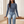 Maribel long sleeve crop top in Blue, seated on an oak bench in a bright room