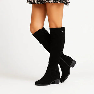 Marlene knee high suede boots in Black with a black block heel, worn with a floral skirt