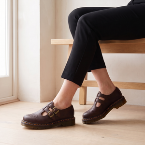 Matilda Mary Jane flats in Brown worn seated on a pale oak bench, showing the ridged sole