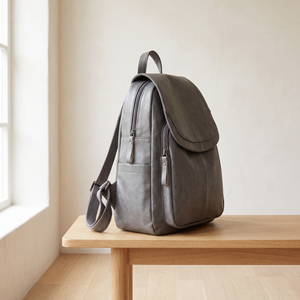 Side view of the Pauline leather backpack in Gray showing the straps, on an oak bench