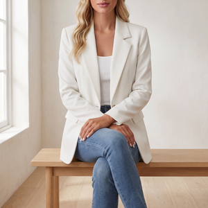 Perrine single button blazer in White, seated on an oak bench in a bright room