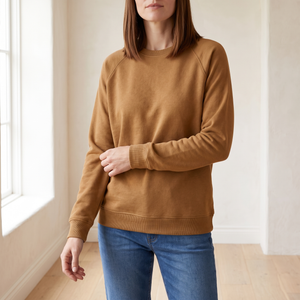 Rita raglan crew neck sweatshirt in Camel by a window in a bright room with plaster walls