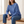 Rita raglan crew neck sweatshirt in Blue worn seated on an oak bench