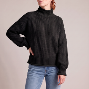 Romane chunky knit turtleneck sweater in Black with jeans on a light gray studio backdrop