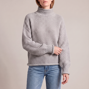 Romane chunky knit turtleneck sweater in Gray with jeans on a light gray studio backdrop