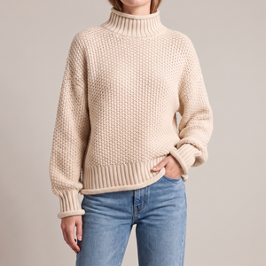 Romane chunky knit turtleneck sweater in White with jeans on a light gray studio backdrop