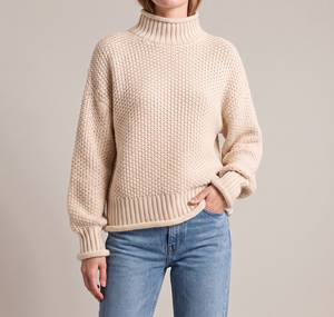 Romane chunky knit turtleneck sweater in White with jeans on a light gray studio backdrop