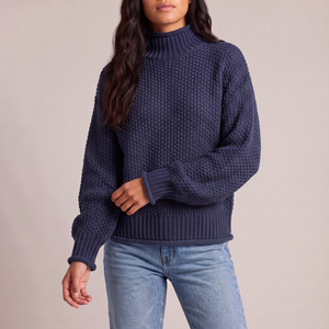 Romane chunky knit turtleneck sweater in Navy Blue with jeans on a light gray studio backdrop