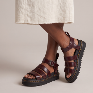 Soledad platform sandals in Burgundy with one foot crossed over the other on a light gray studio backdrop