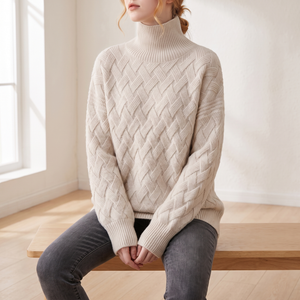 Verity lattice knit turtleneck sweater in Beige worn seated on an oak bench, showing the ribbed cuffs